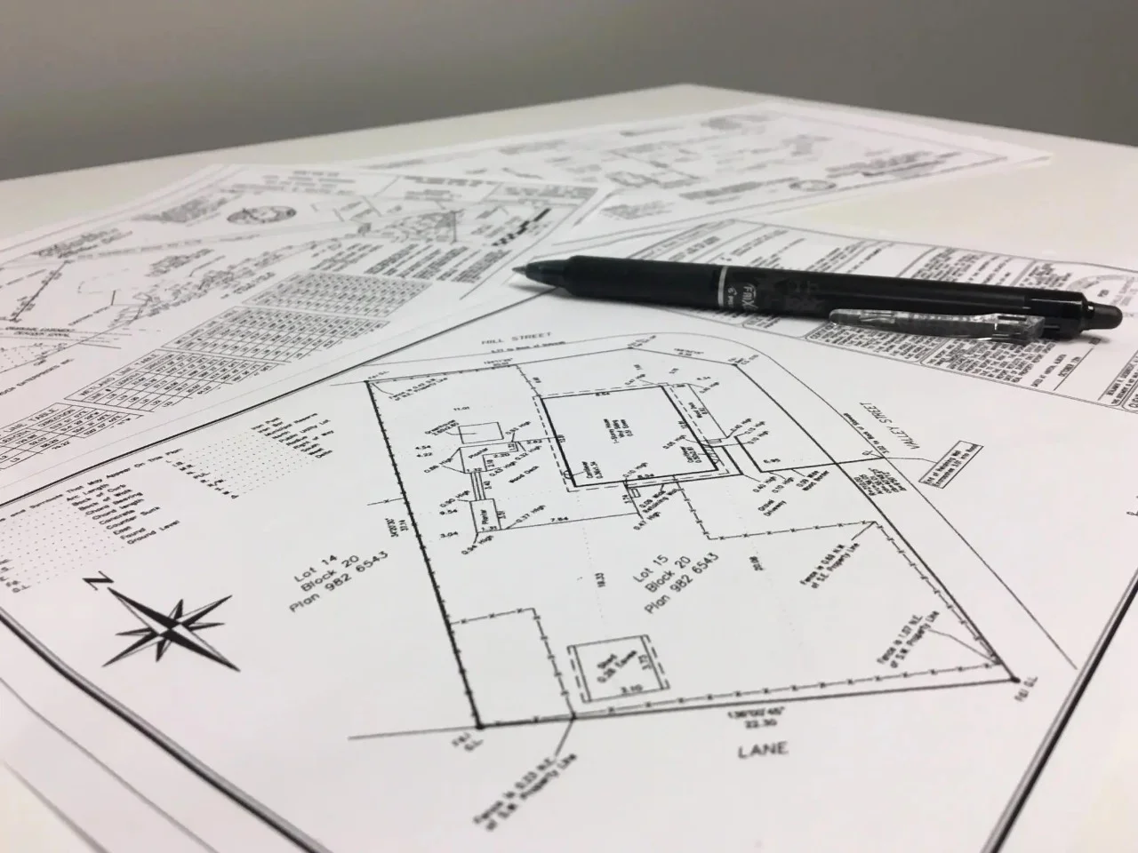 Close-up of architectural blueprints on a table with a black pen resting on top, showing floor plans and site layout.